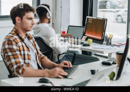 Rückansicht des afrikanischen amerikanischen Programmierer mit Computer mit online Handel auf dem Monitor in der Nähe von Kollege im Büro Stockfoto