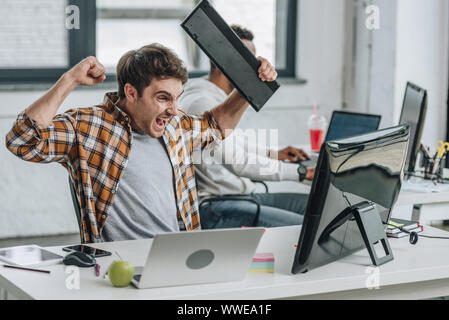 Gereizte Programmierer holding Tastatur und gestikulierend während Com [uter Monitor suchen Stockfoto