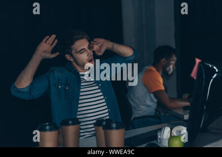 Selektiver Fokus der junge Programmierer Gähnen beim Sitzen in der Nähe der afrikanischen amerikanischen Kollegen Stockfoto