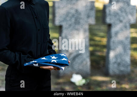 7/8-Ansicht von Frau mit der amerikanischen Flagge auf dem Friedhof Stockfoto