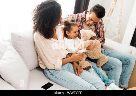 Afrikanische amerikanische Familie sitzt auf dem Sofa und lächelt während Vater spielt mit Tochter Stockfoto