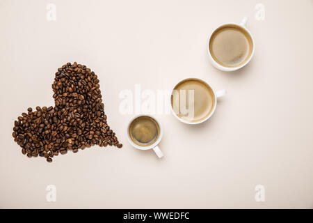 Blick von oben auf die Tassen mit Kaffee in der Nähe von Herz aus Kaffee Körner auf beigen Hintergrund Stockfoto