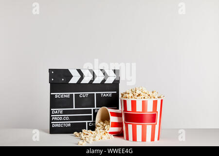 Popcorn in gestreiften Eimer in der Nähe der Klappe isoliert auf Grau Stockfoto