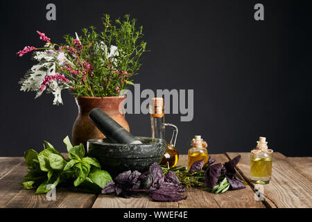 Grau Mörser in der Nähe von Clay Vase mit Kräutern und kleine Flaschen auf Holztisch isoliert auf Schwarz Stockfoto