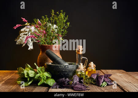 Grau Mörser in der Nähe von Clay Vase mit frischen Wildblumen und Kräutern auf Holztisch isoliert auf Schwarz Stockfoto