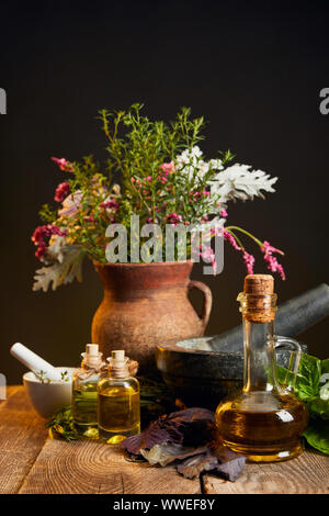 Ton Vase mit frischen Kräutern und Blumen in der Nähe von Mörser und Stößel und Flaschen auf hölzernen Tisch Stockfoto