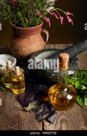 Mörser mit Pistill, Flaschen mit Öl und Ton Vase mit frischen Blumen auf Holz- Oberfläche isoliert auf Schwarz Stockfoto