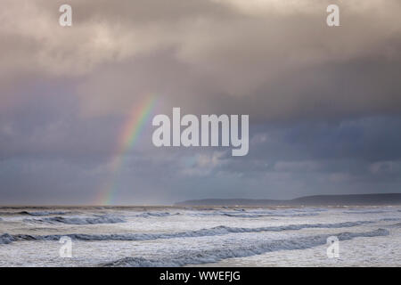 Stürmische Meere bei Westward Ho in North Devon, England mit Regenbogen am Horizont. Stockfoto