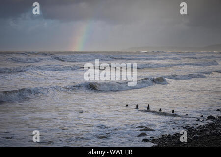 Stürmische Meere bei Westward Ho in North Devon, England mit Regenbogen am Horizont. Stockfoto