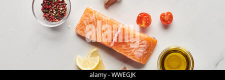 Blick von oben auf die rohen Lachs Steak in der Nähe von Lemon, Tomaten, Knoblauch, Öl und Pfefferkörner in Schalen auf Marmor tisch, Panorama-Aufnahme ein. Stockfoto