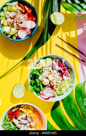 Poke Schüssel sind te letzte Trend in der Lebensmittelindustrie, eine Schüssel mit Gemüse und Lachs auf einem gelb rosa Hintergrund mit riesigen monstera Blatt um. Stockfoto