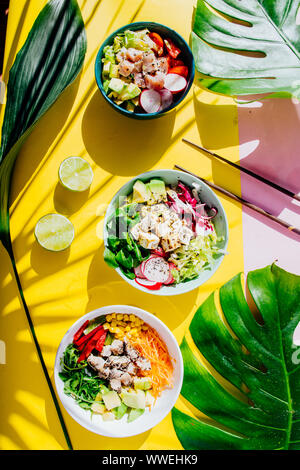 Poke Schüssel sind te letzte Trend in der Lebensmittelindustrie, eine Schüssel mit Gemüse und Lachs auf einem gelb rosa Hintergrund mit riesigen monstera Blatt um. Stockfoto