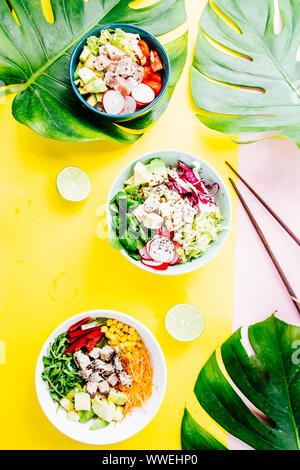 Poke Schüssel sind te letzte Trend in der Lebensmittelindustrie, eine Schüssel mit Gemüse und Lachs auf einem gelb rosa Hintergrund mit riesigen monstera Blatt um. Stockfoto