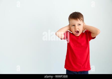 Schreienden kleinen Jungen mit autistischen Störungen, die Ohren auf hellen Hintergrund Stockfoto