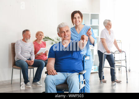 Junge Betreuer nach deaktiviert reifer Mann im Pflegeheim suchen Stockfoto