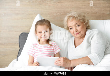 Süße kleine Mädchen mit Großmutter mit Tablet PC im Bett zu Hause Stockfoto