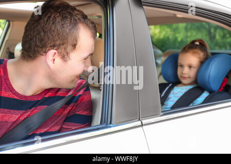 Mann, der mit seiner Tochter in Sicherheit Sitz angeschnallt Stockfoto