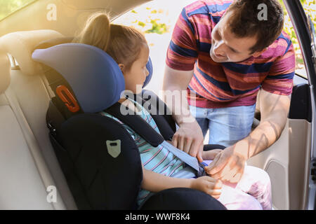 Vater Knickung seine kleine Tochter im Auto Kindersitz Stockfoto