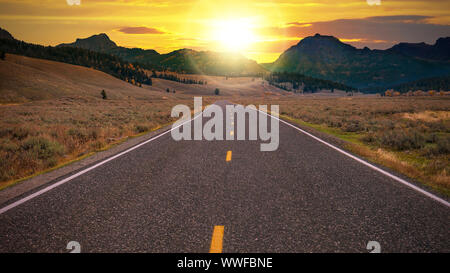 Zweispurigen Landstraße in Richtung einer goldenen Sonnenaufgang über einem Pass am Horizont. Konzeptionelle für Freiheit, ein frischer neuer Tag, neue Möglichkeiten. Stockfoto