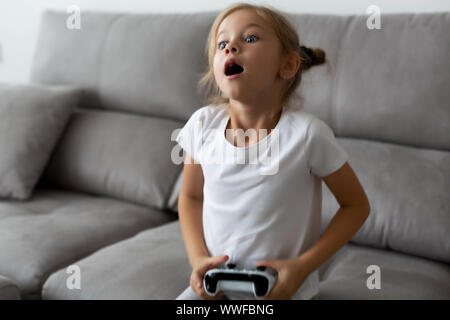 Emotionale Portrait von blondes Mädchen in Weiß gekleidet. wenig Spieler sitzt auf einem Sofa Stockfoto