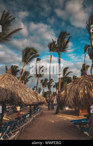 Sonnenuntergang Licht auf Punta Cana Strand mit Liegestühlen, Sonnenschirmen und Palmen. Landschaft von Paradise Tropical Island Beach mit perfekter Blau sonnig Stockfoto