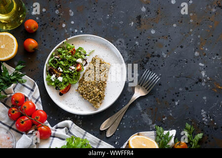 Gebackener Wolfsbarsch würzigen Panade mit frischen Salat. Ein Beispiel für ein ausgewogenes Mittagessen. Das Konzept der richtige Ernährung. Leckere, gesunde und einfache Gerichte. Stockfoto