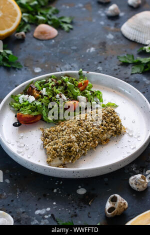 Gebackener Wolfsbarsch würzigen Panade mit frischen Salat. Ein Beispiel für ein ausgewogenes Mittagessen. Das Konzept der richtige Ernährung. Leckere, gesunde und einfache Gerichte. Stockfoto