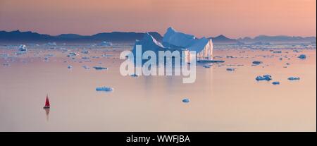 Kleine rote Segelboot Kreuzfahrt unter schwimmende Eisberge in der Diskobucht Gletscher mitternachtssonne Saison von polaren Sommer. Ilulissat, Grönland. Unesco Stockfoto