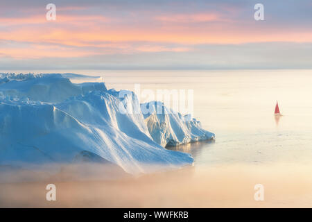 Kleine rote Segelboot Kreuzfahrt unter schwimmende Eisberge in der Diskobucht Gletscher mitternachtssonne Saison von polaren Sommer. Ilulissat, Grönland. Unesco Stockfoto