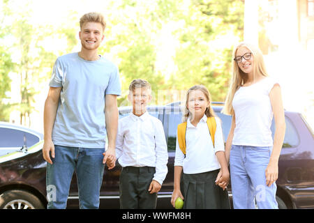 Eltern mit ihren kleinen Kindern in der Nähe von Autos vor der Schule Stockfoto