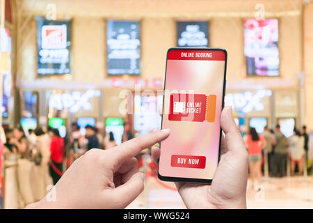 Mockup Handy hand mit Smartphone Kinokarten mit unscharfen Bild der Ticketverkauf zu kaufen Zähler bei Kino mit grafisches Symbol, online Stockfoto