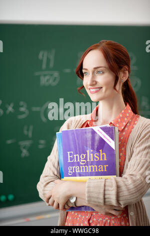 Strahlende Lehrer holding Bücher stehen im Klassenzimmer Stockfoto