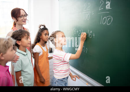 Intelligentes Mädchen schreiben Sie Zahlen auf der Tafel bei der Klasse Math Stockfoto