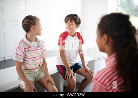 Mädchen mit Ohrhörer am Hals sprechen mit ihrer Klassenkameradin Stockfoto