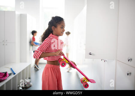 Schulmädchen tragen gestreifte Shirt, Penny board im Schließfach Stockfoto