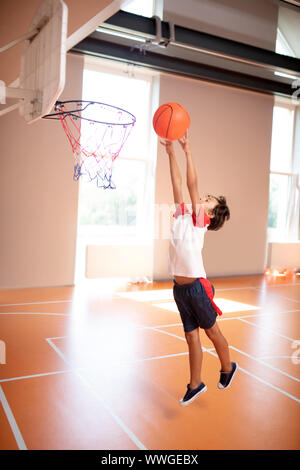 Schüler tragen Sport Kleidung werfen Ball in Warenkorb Stockfoto