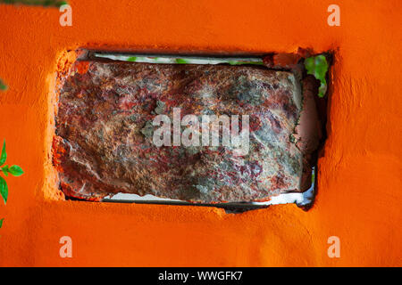 Ein natürlicher Stein von einer rechteckigen Form in Form eines Ziegelstein in die vertikale Bohrung eines orange Beton Wand eingefügt. Bau Konzept. Stockfoto