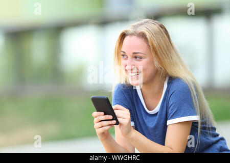 Happy teenage Girl holding Telefon bei sidesitting in einem Campus der Universität Suchen Stockfoto