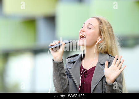 Happy teenage Mädchen Karaoke singen mit Smart Phone und Ohrhörer im Freien Stockfoto