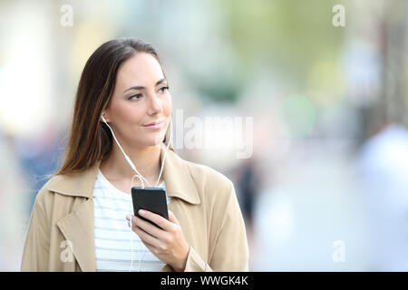 Vorderansicht Portrait von eine nachdenkliche Frau trägt Ohrhörer zu Hören von Musik auf dem Handy auf der Straße Stockfoto