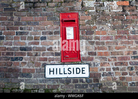 Alte rote englische Royal Mail wall Post Box in einer gemauerten Wand über ein Straßenschild mit dem Namen 'Hügel' Stockfoto