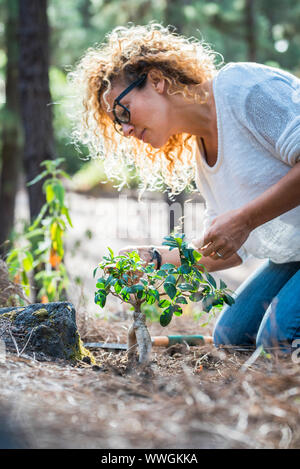 Umwelt Konzept mit schönen lockigen Jungen erwachsenen Frau kümmern sich um neue Pflanzen im Wald - der Planet und nette Leute speichern Stopp der Abholzung Stockfoto