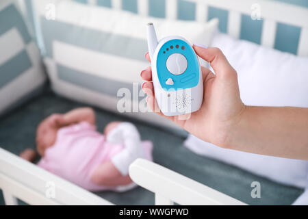 Mutter Holding radio Nanny in der Nähe von Bed mit schlafenden Baby Stockfoto