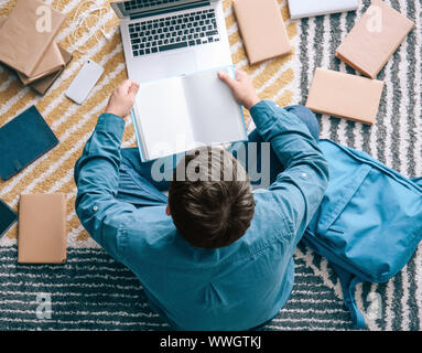 Asiatische Kursteilnehmer mit einer Menge Bücher und Laptop Vorbereitung auf die Prüfung zu Hause Stockfoto