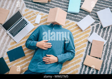 Asiatische Kursteilnehmer mit einer Menge Bücher und Laptop Vorbereitung auf die Prüfung zu Hause Stockfoto