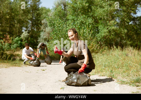 Süße Herzen die Rettung des Planeten. Gruppe von Freiwilligen aufräumen Müll am Strand in sonniger Tag. Junge Männer und Frauen kümmern sich um die Natur und die Umwelt, die Flaschen und Gebinde entfernt. Konzept der Ökologie. Stockfoto