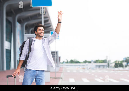 Jungen Kerl in der Nähe von Flughafen, hebt die Hand und versucht Auto zu stoppen Stockfoto