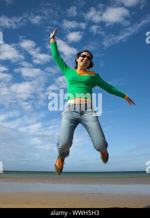 Junge schöne Frau, die einen grossen Sprung am Strand Stockfoto