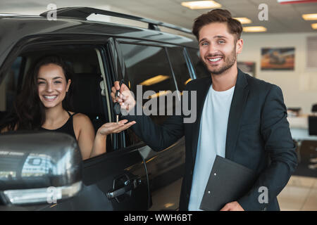 Schöner mann Manager gibt Autoschlüssel zu schöne Brünette Frau Client nach der erfolgreichen Einzelhandel Angebot in der Händlerniederlassung entfernt in der Nähe von neuen SUV Stockfoto