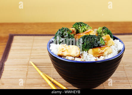 Vegetarisches Gericht von gebratenem Tofu, Brokkoli und Orangensauce mit Stäbchen rühren. Selektiver Fokus auf Lebensmittel mit einigen auf den unteren Teil des Bildes. Stockfoto